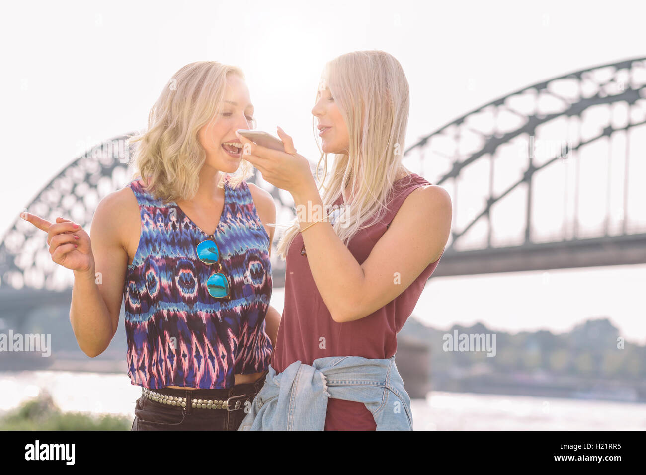 Two young women with cell phone at riverbank Stock Photo