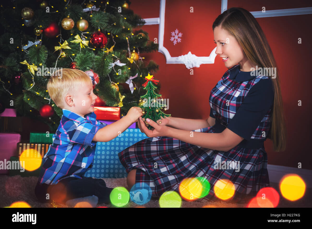 Young mother and her son near a Christmas tree in the decorated room with gifts. Stock Photo