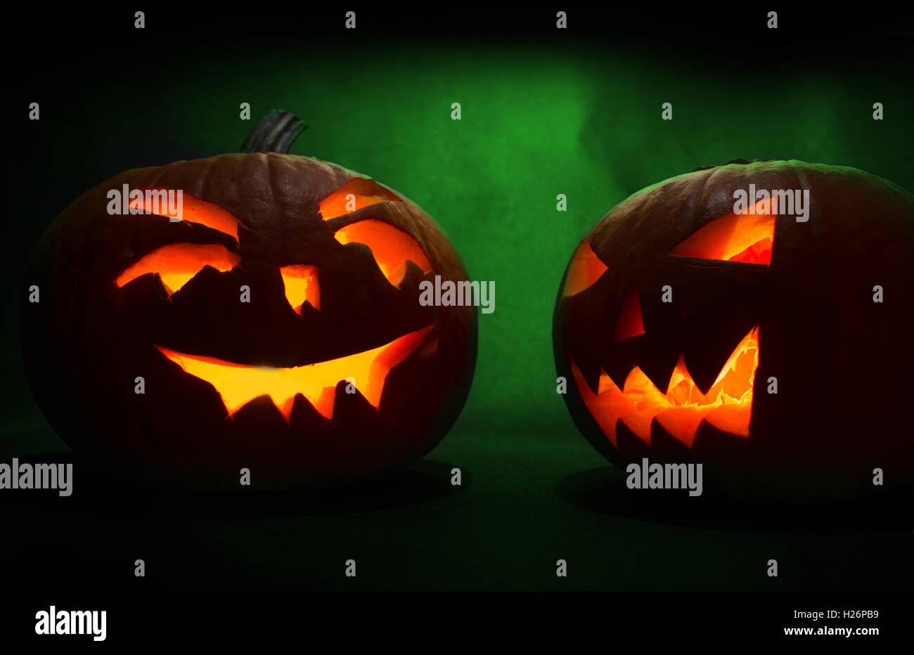 Two carved faces of pumpkins glowing on Halloween on green background ...