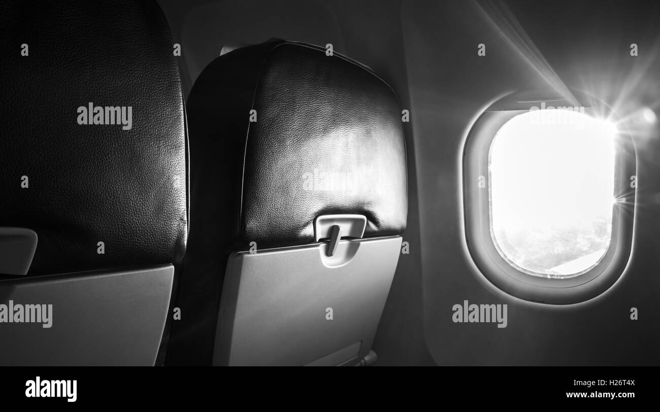 Passenger plane interior fragment. Main cabin chairs with folding table and glowing porthole with natural sunlight lens flare. B Stock Photo