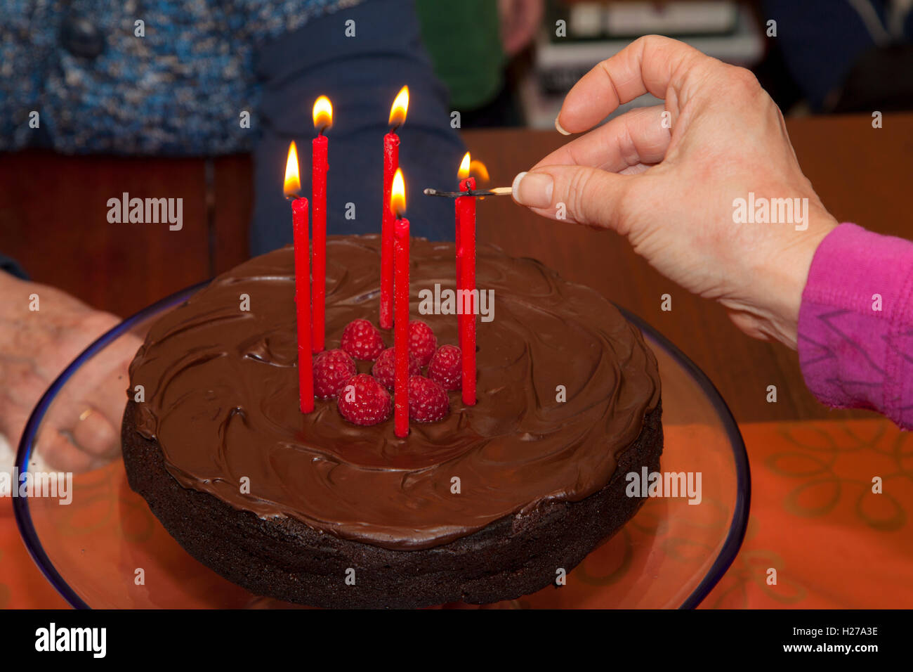 Five candles being lit on chocolate frosted birthday cake garnished with raspberries. St Paul Minnesota MN USA Stock Photo