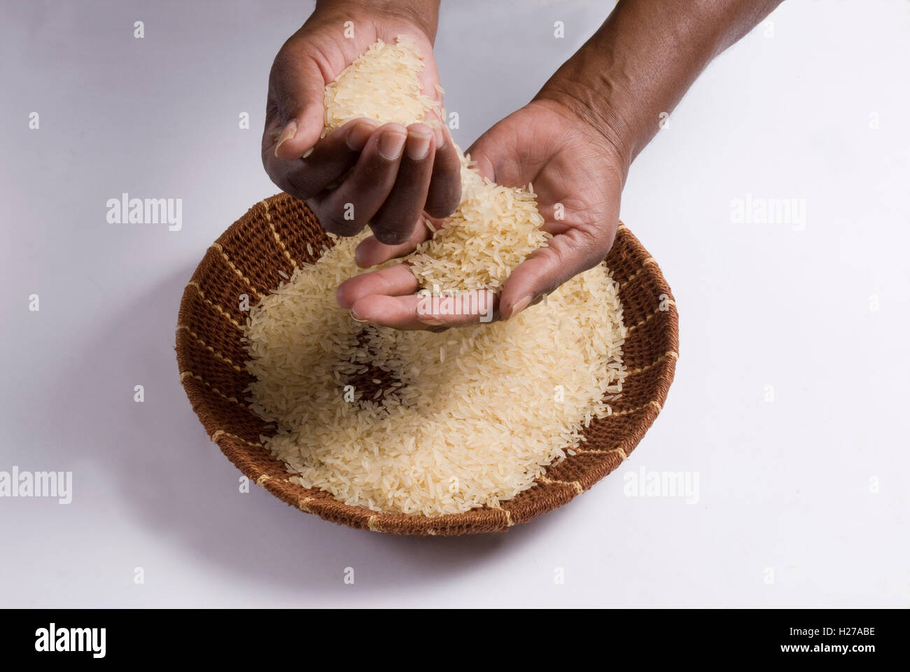 African's hands pouring rice over a woven grass bowl, Studio shot on white background. Stock Photo