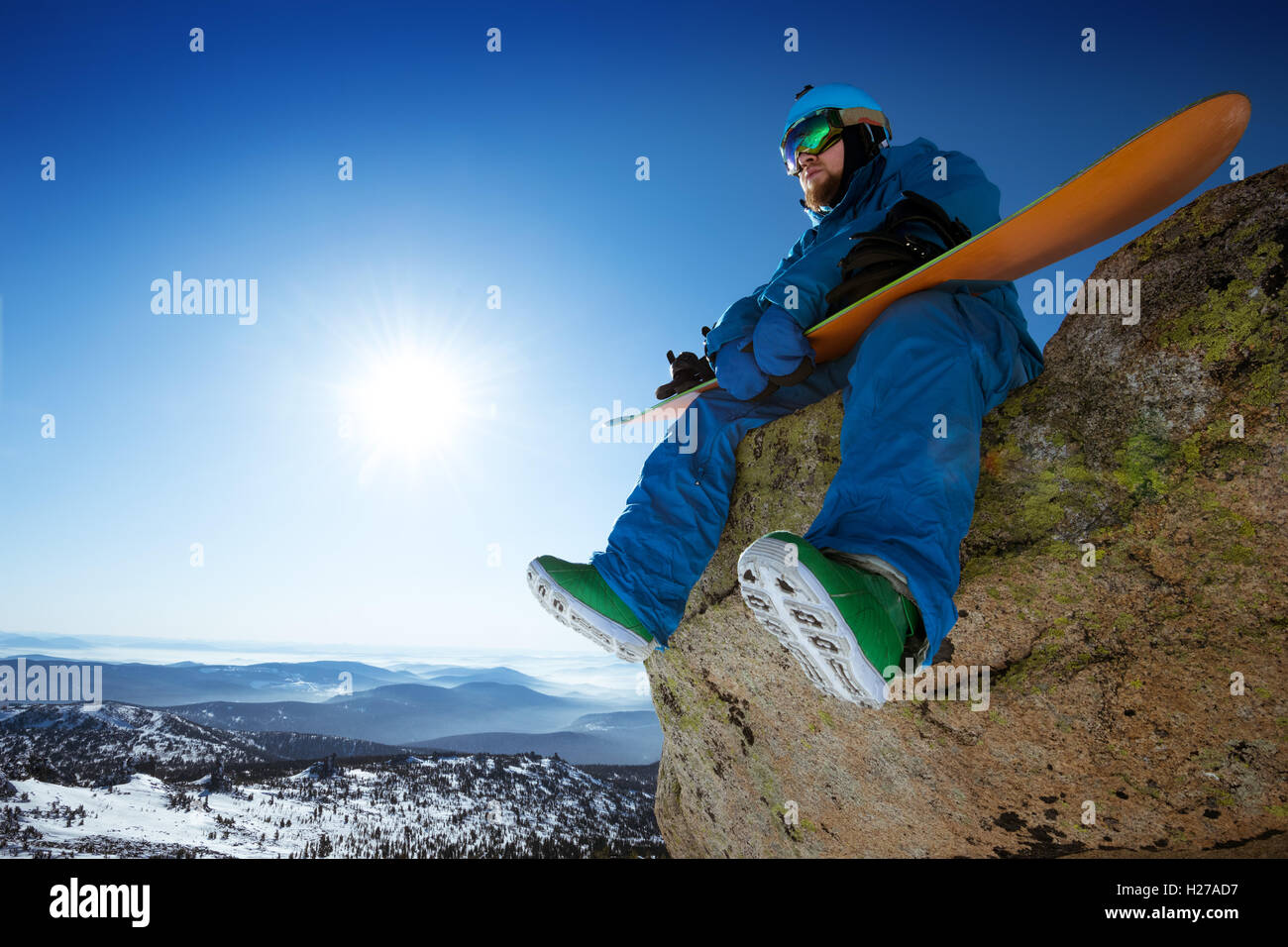 Snowboarder sits on blue sky backdrop in mountains Stock Photo