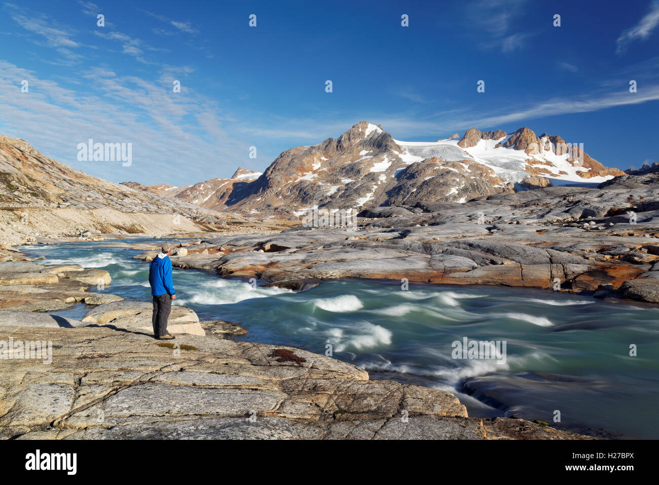 Hiker looking over glacial melt river and mountains, Sammileq Fjord, Ammassalik Island, East Greenland Stock Photo