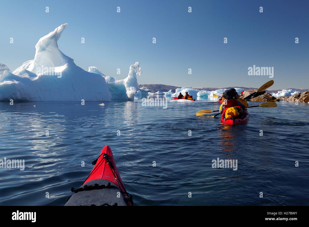 Sea kayakers paddling among icebergs on Sermilik Fjord near settlement of Tiniteqilaq, East Greenland Stock Photo