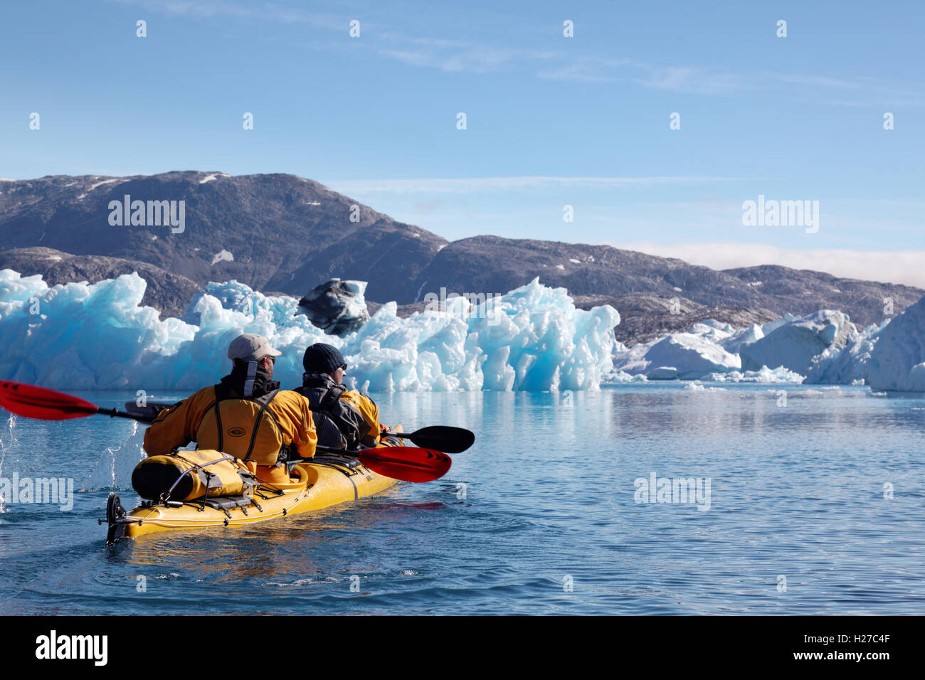 Sea kayakers paddling among icebergs on Sermilik Fjord near settlement of Tiniteqilaq, East Greenland Stock Photo