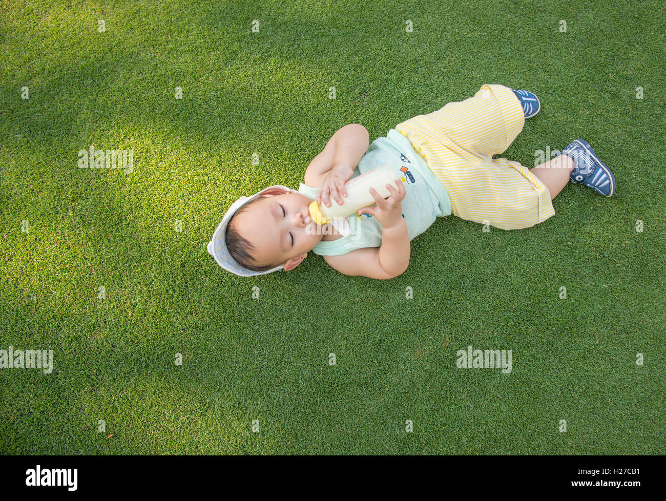 Adorable Asian baby boy laying on the grass field and  drinking milk from bottle when picnic with family in the out door park, u Stock Photo