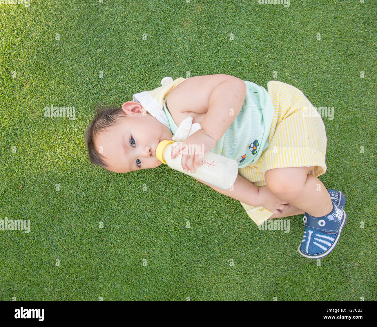 Adorable Asian baby boy laying on the grass field and  drinking milk from bottle when picnic with family in the out door park, u Stock Photo