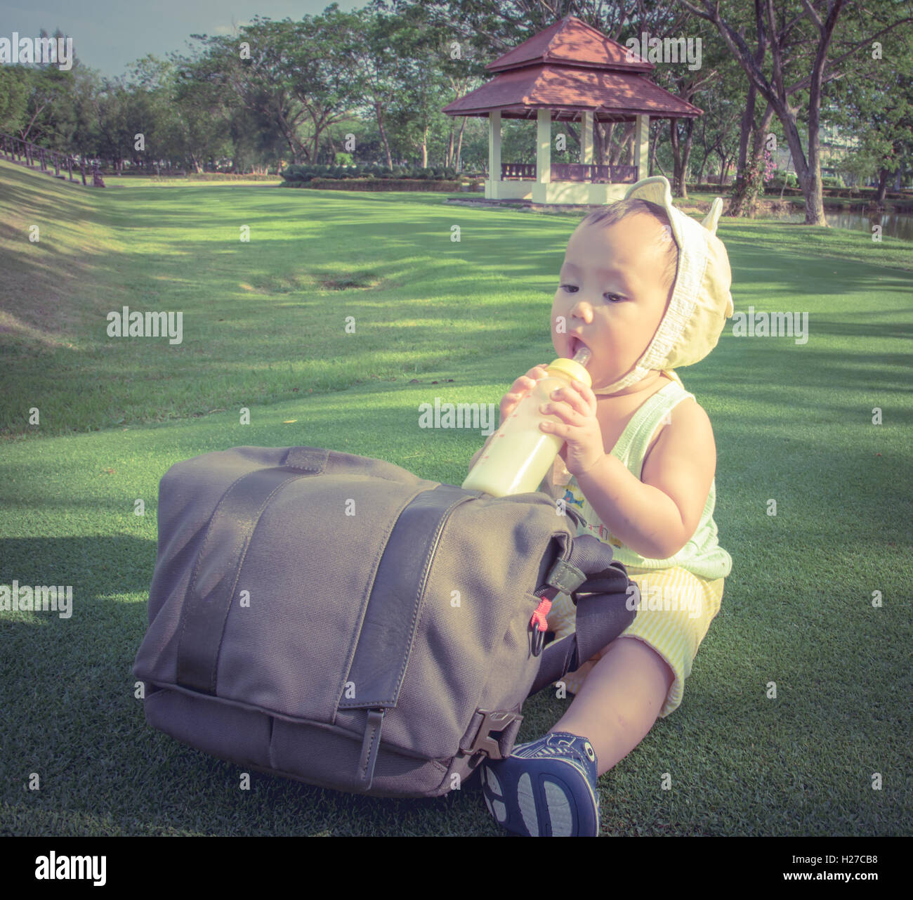 Adorable Asian baby boy drinking milk from bottle when picnic with family in the out door park, Soft pastel color effect Stock Photo