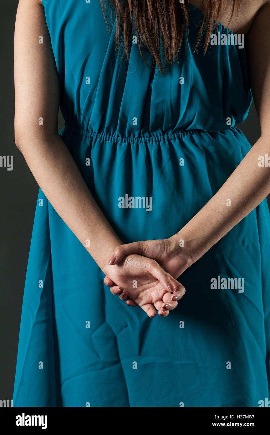 Rear view close up of a woman in blue dress standing with hands behind ...