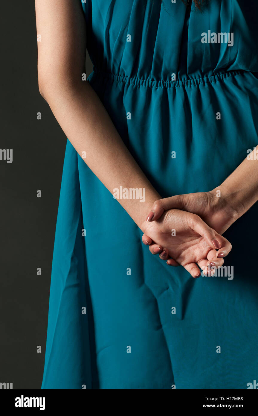Rear view close up of a woman in blue dress standing with hands behind ...
