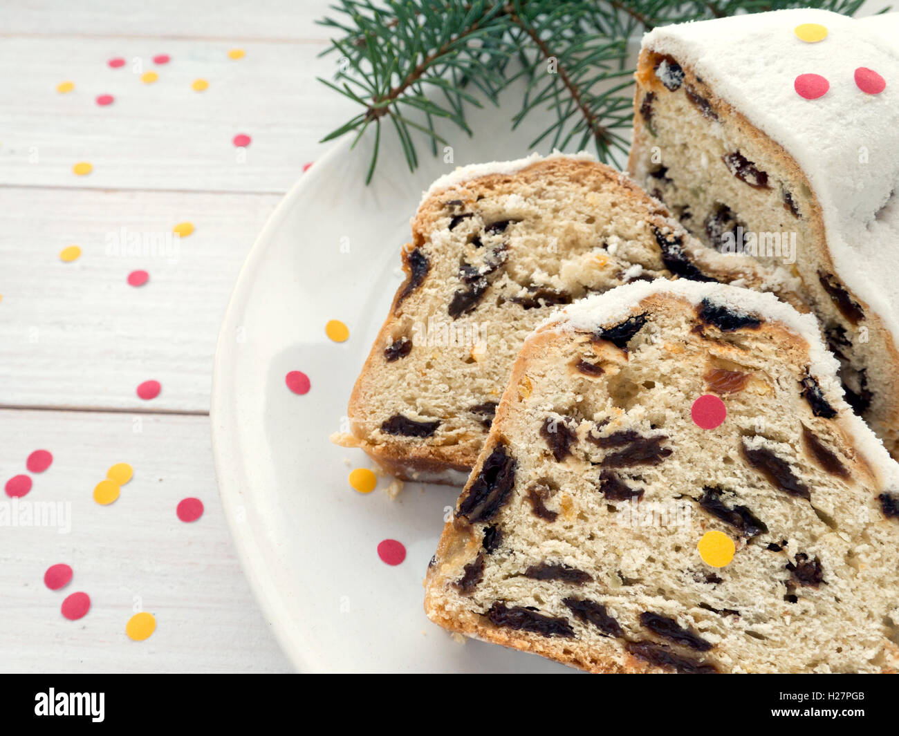 Stollen German Christmas cake on the white plate and blue spruce branches on the white wooden planks sprinkled with confetti Stock Photo