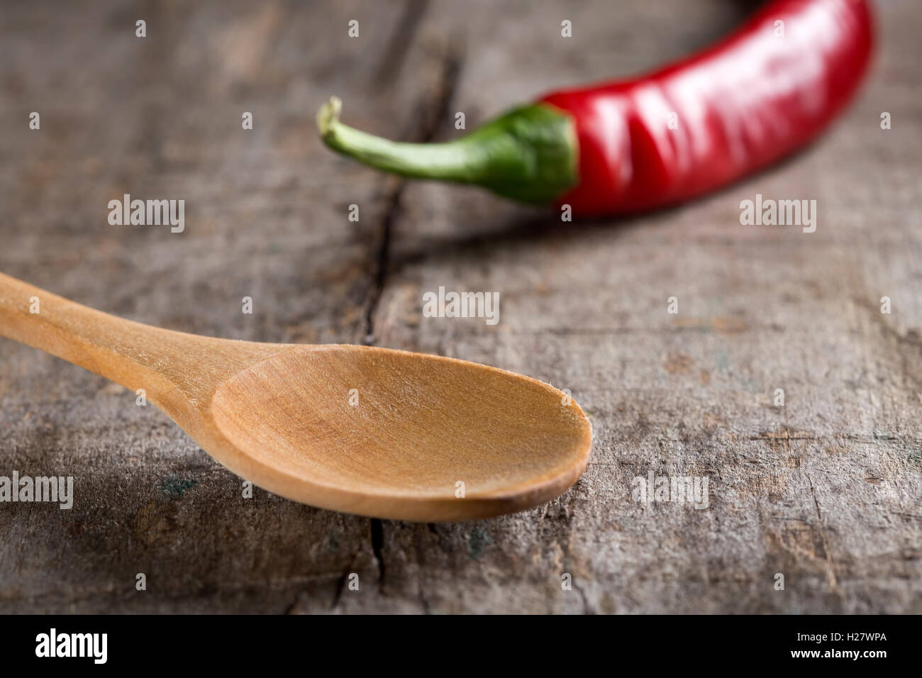 Close up of empty wooden spoon on table and one red hot pepper in background Stock Photo