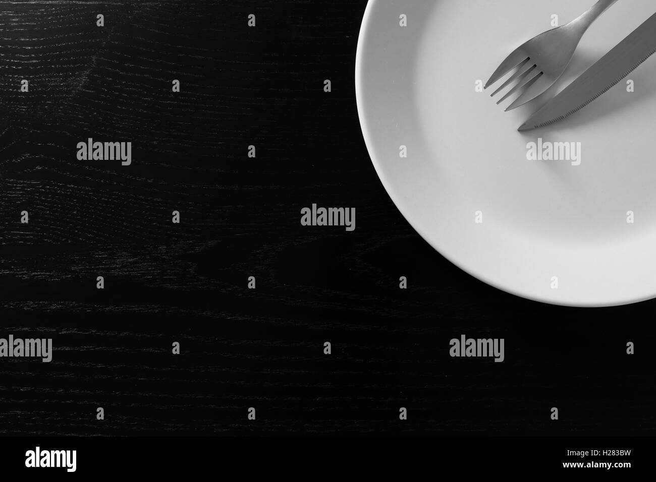 Empty white plate on black wooden table. Kitchen tools close up Stock Photo