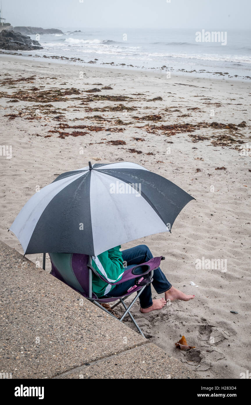 This woman is very dedicated to be at the beach.So a little rain, and fog is not going to keep her from it on her vacation. Stock Photo