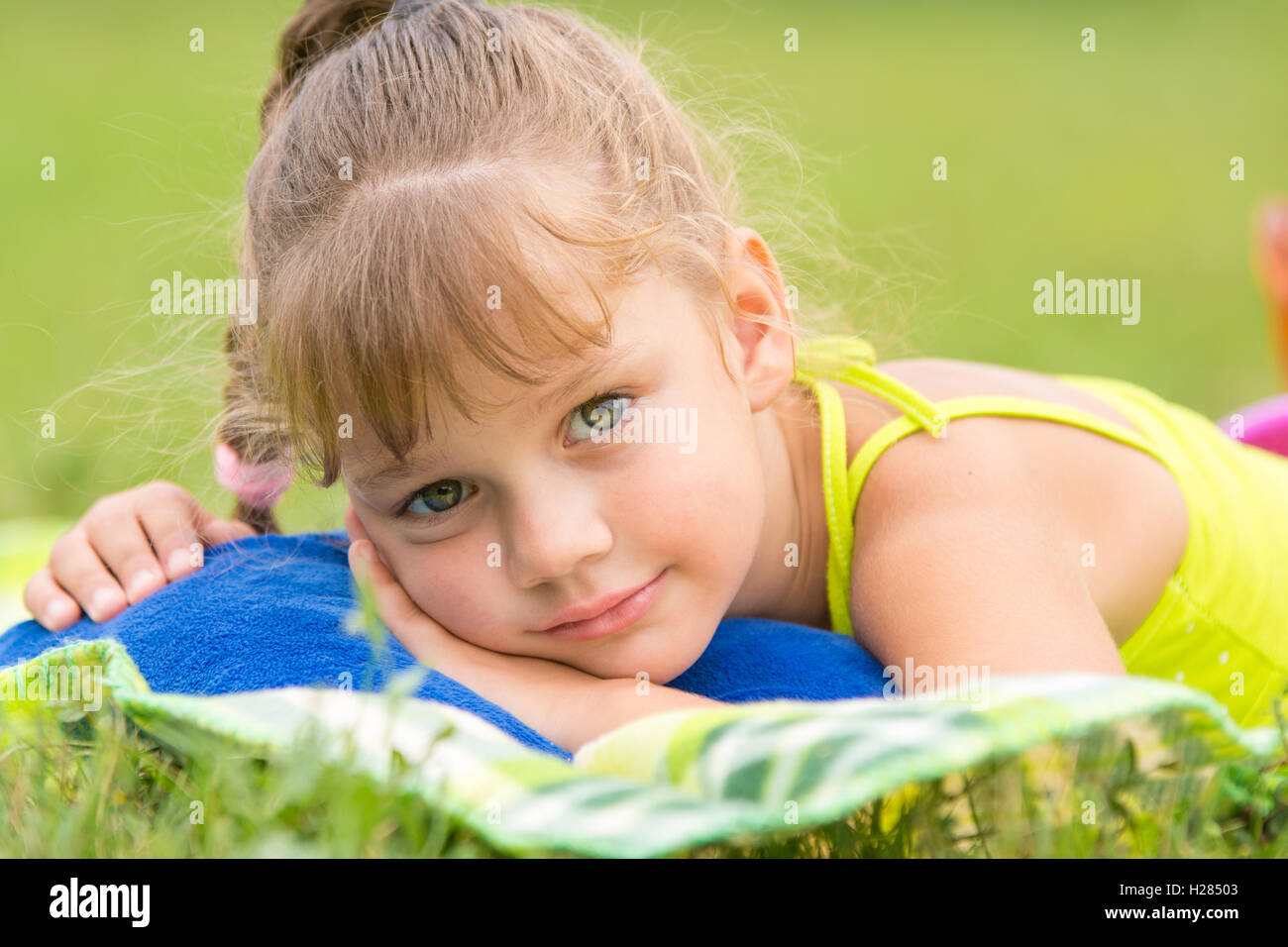 Five-year girl lies on a bed on a green meadow and touching looking to the frame Stock Photo