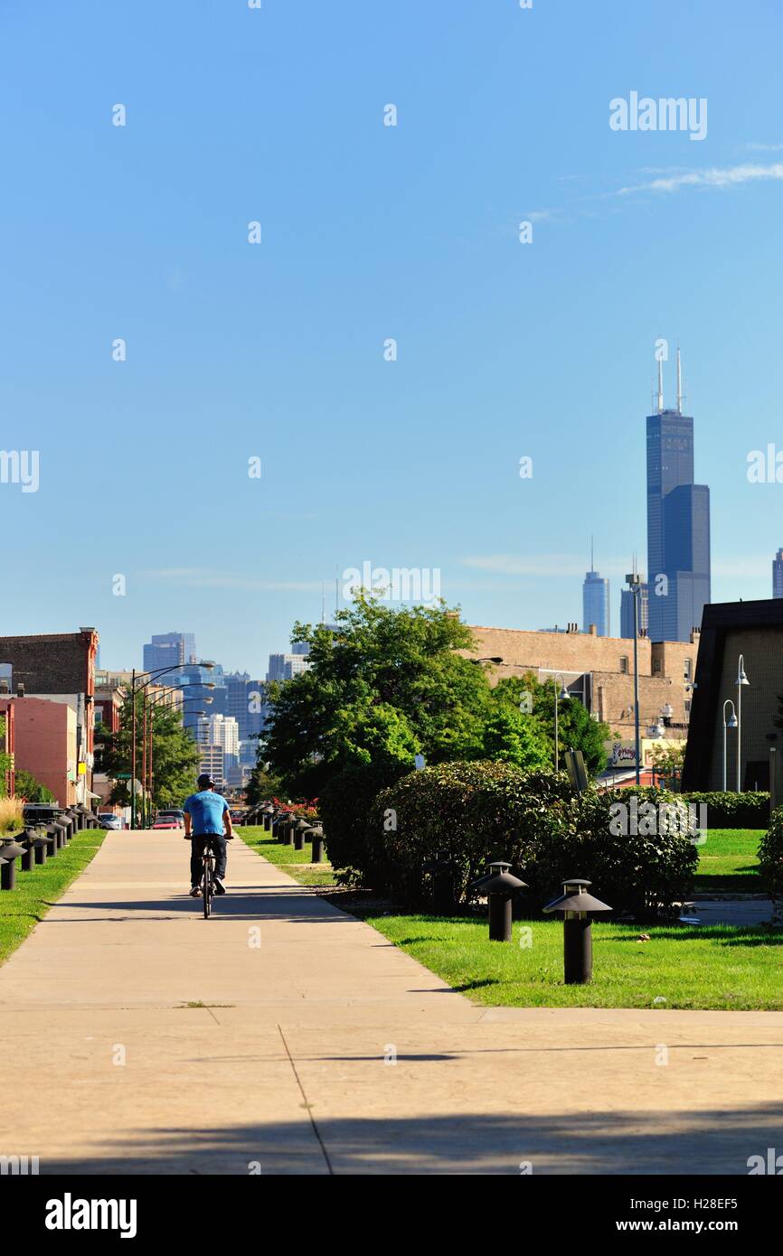 A lone cyclist traveling through a park and plaza adjacent to Chicago's Benito Juarez High School. Chicago, Illinois, USA. Stock Photo