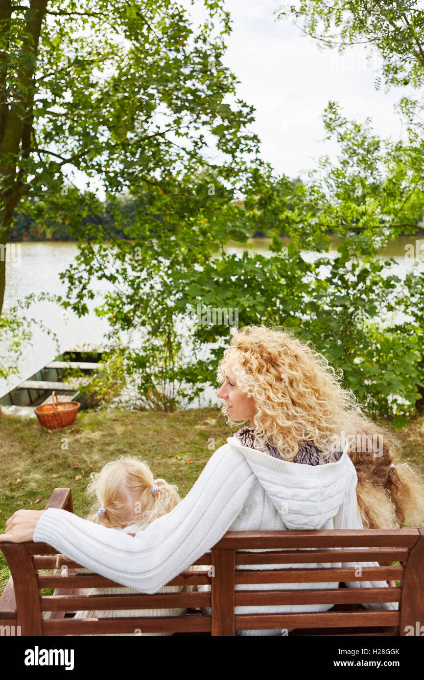 Mother with two kids at lake shore sitting on bench Stock Photo