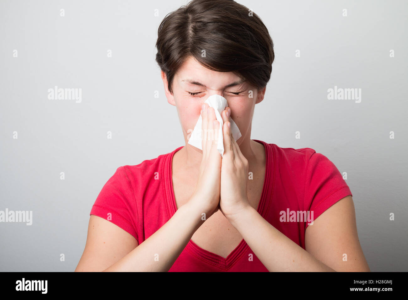 Young woman blowing her nose too hard Stock Photo