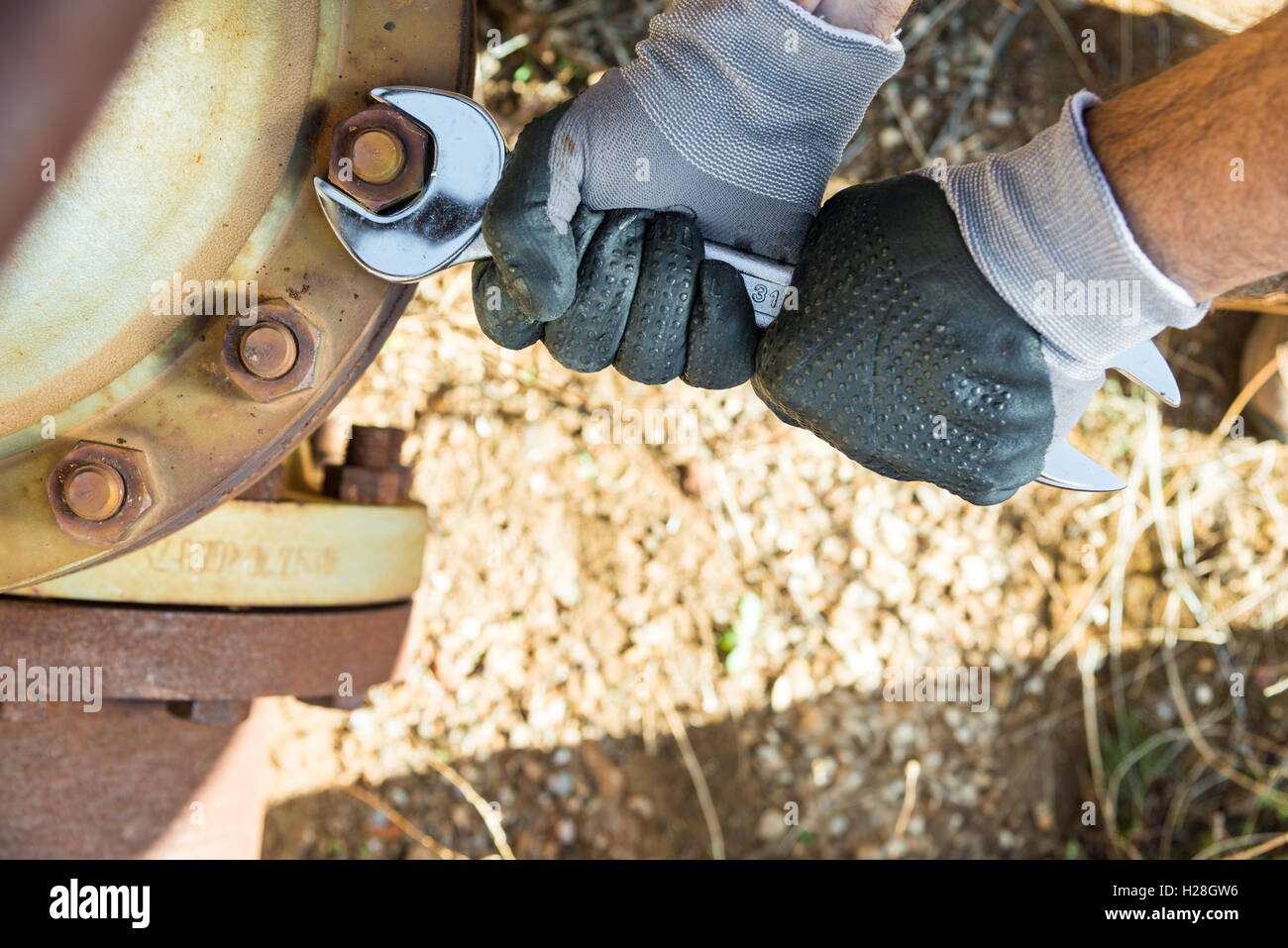 Hands with Work Gloves Holding a Wrench and Tighten very Rusty Bolts Stock Photo