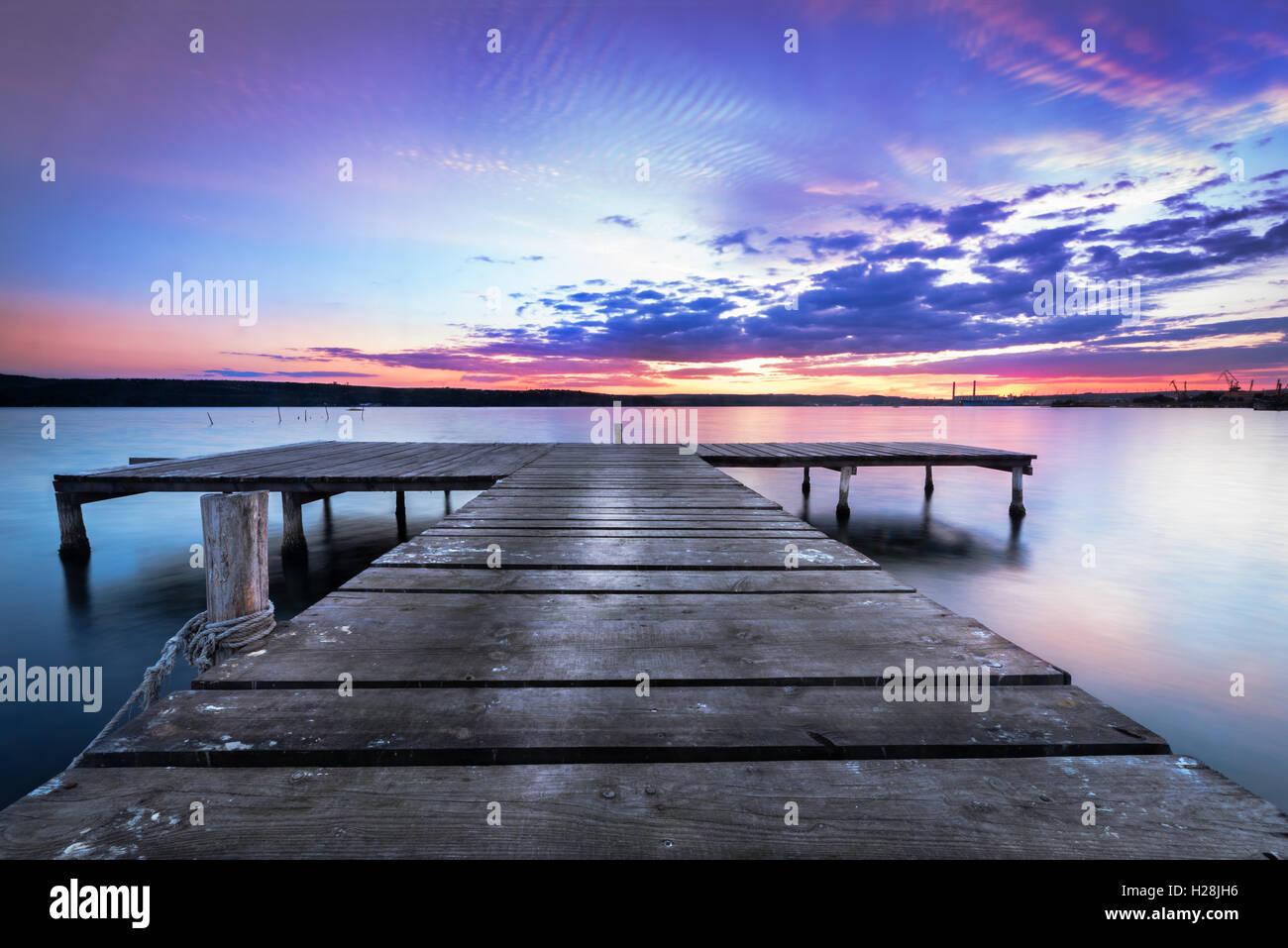 Wooden pier on a blue lake sunset and smooth reflection on water. Stock Photo