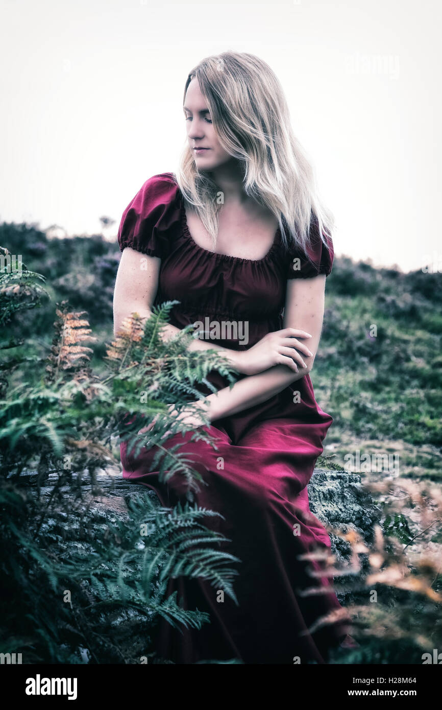 a blonde woman in a red dress is sitting outside in the nature Stock Photo