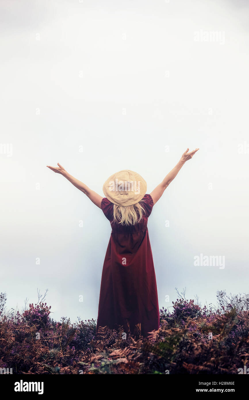 a woman in a red dress with a hat is raising her arms Stock Photo