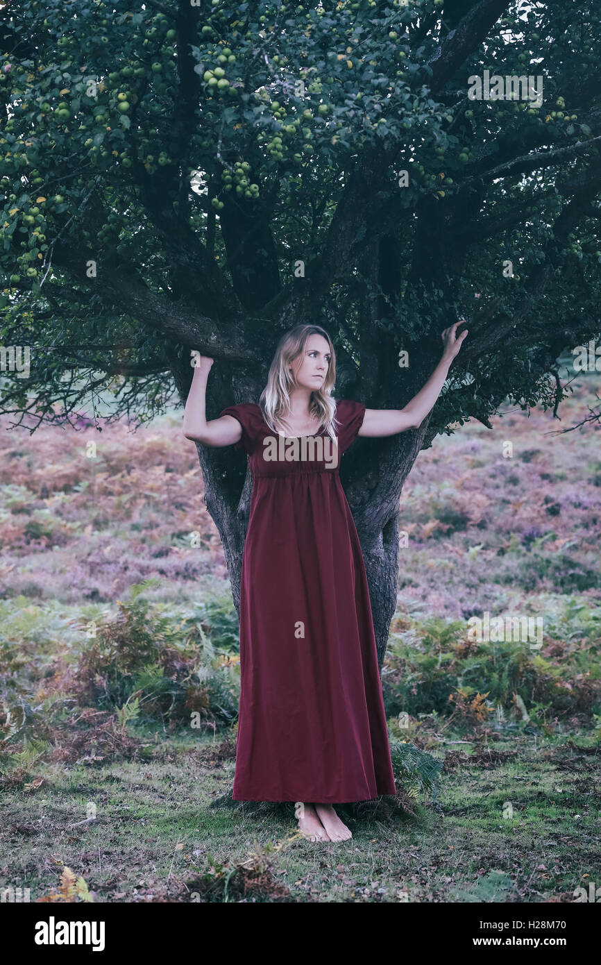 a blonde woman with a red dress is standing under a tree Stock Photo