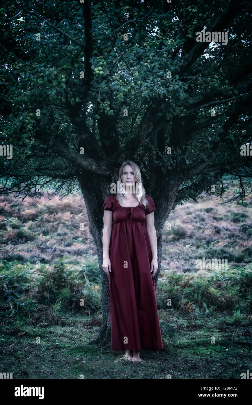 a woman in a red dress is standing under a tree Stock Photo