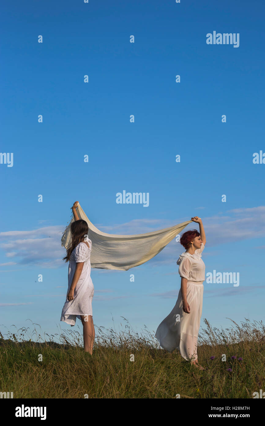 two girls in white dresses are holding a shawl in the wind Stock Photo