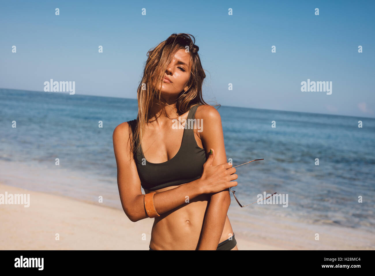 Portrait of sensuous young woman in bikini on the beach. Female model posing in swimsuit on the sea shore. Stock Photo