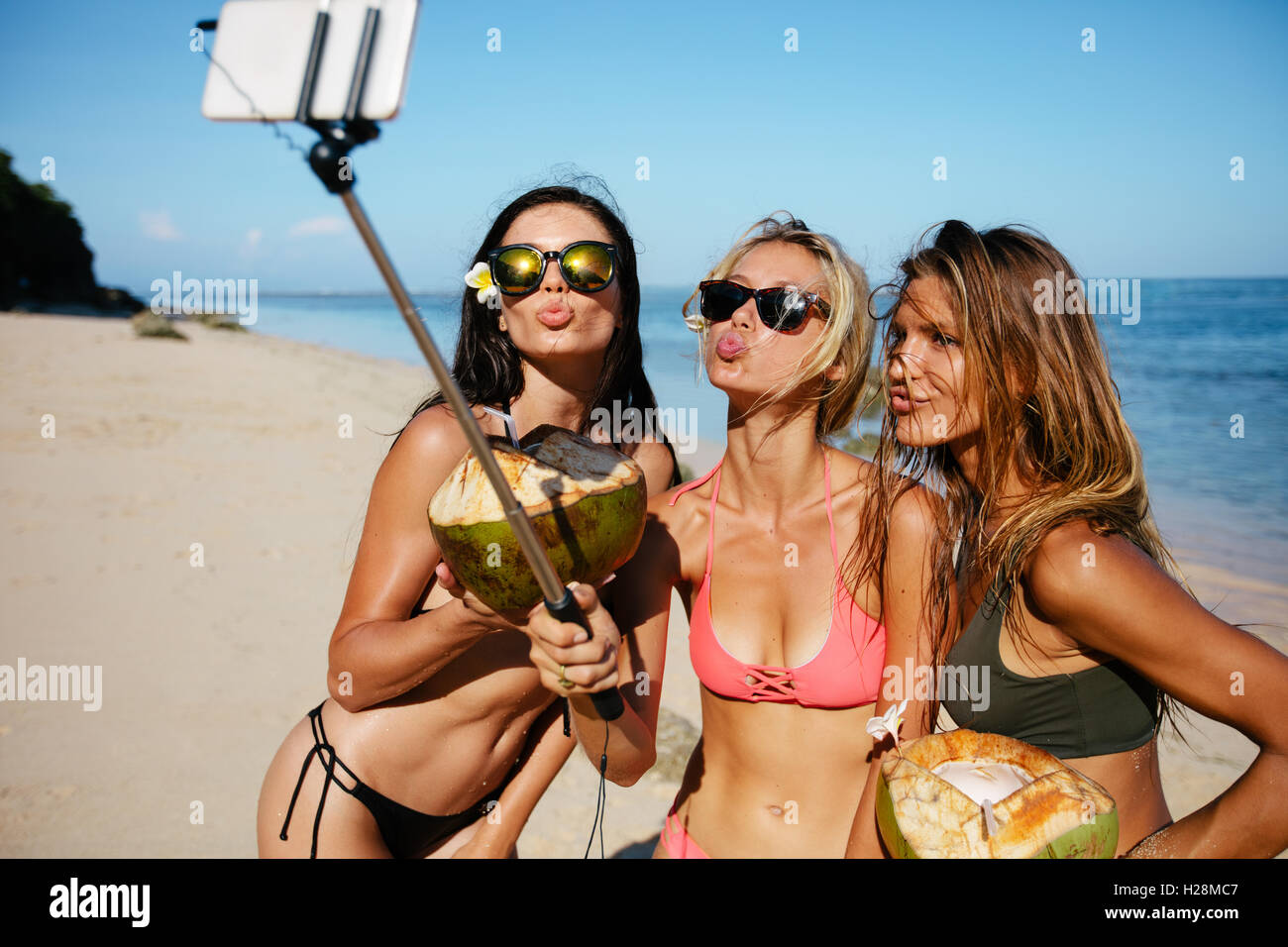 Three young women in swimsuit on the beach enjoying holidays and taking self portrait selfie stick. Group of female friends with Stock Photo