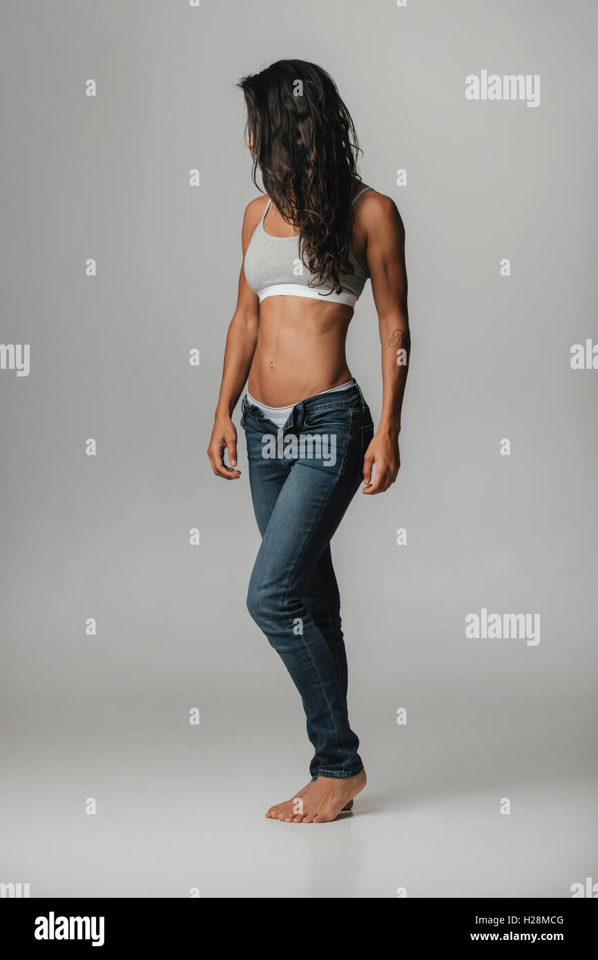 Strong beautiful tanned woman wearing halter top and unzipped jeans covers face with her long brown hair Stock Photo