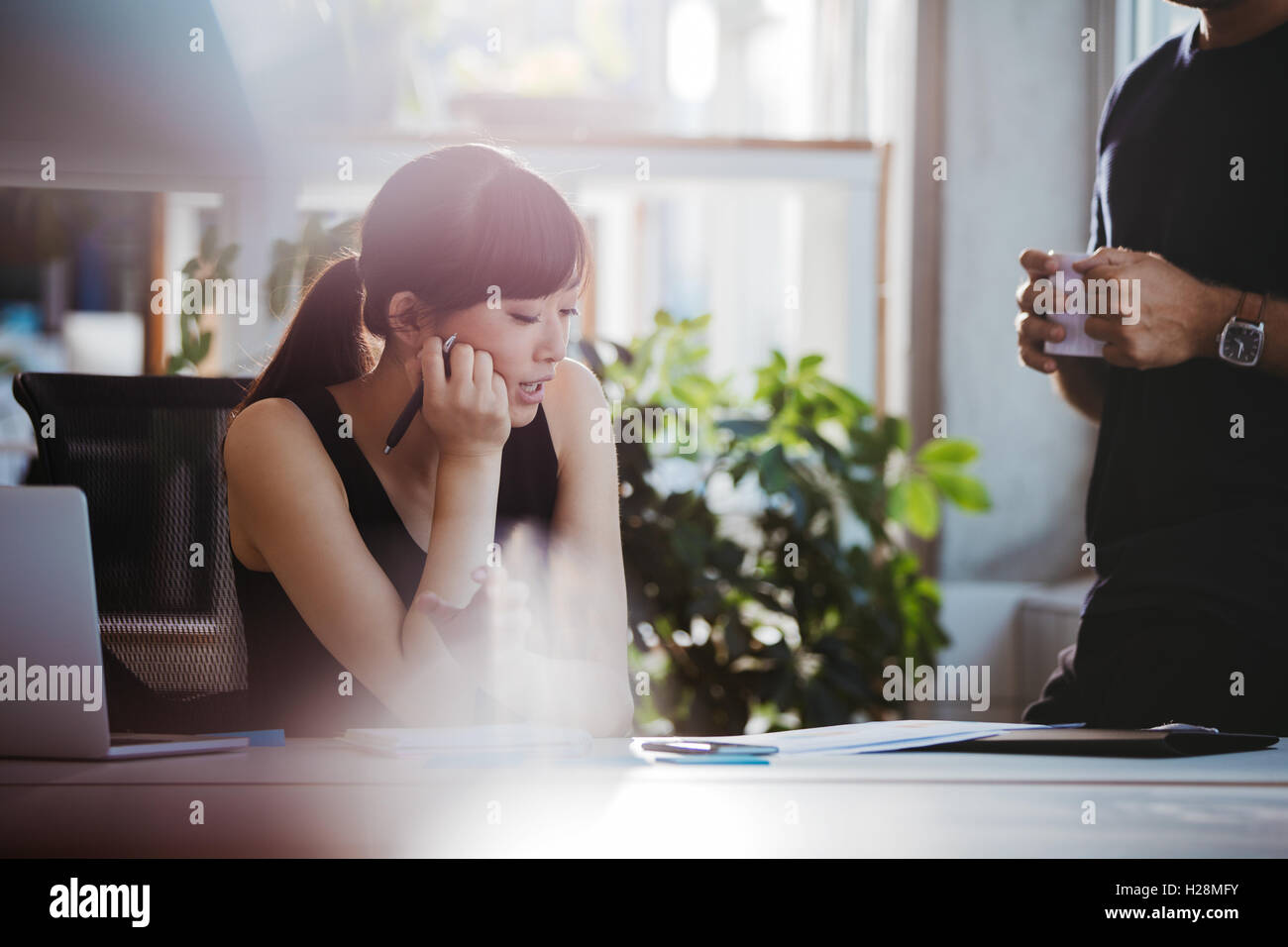 Shot of young woman sitting at her desk and talking with male colleague standing by. Coworkers working together on new business Stock Photo