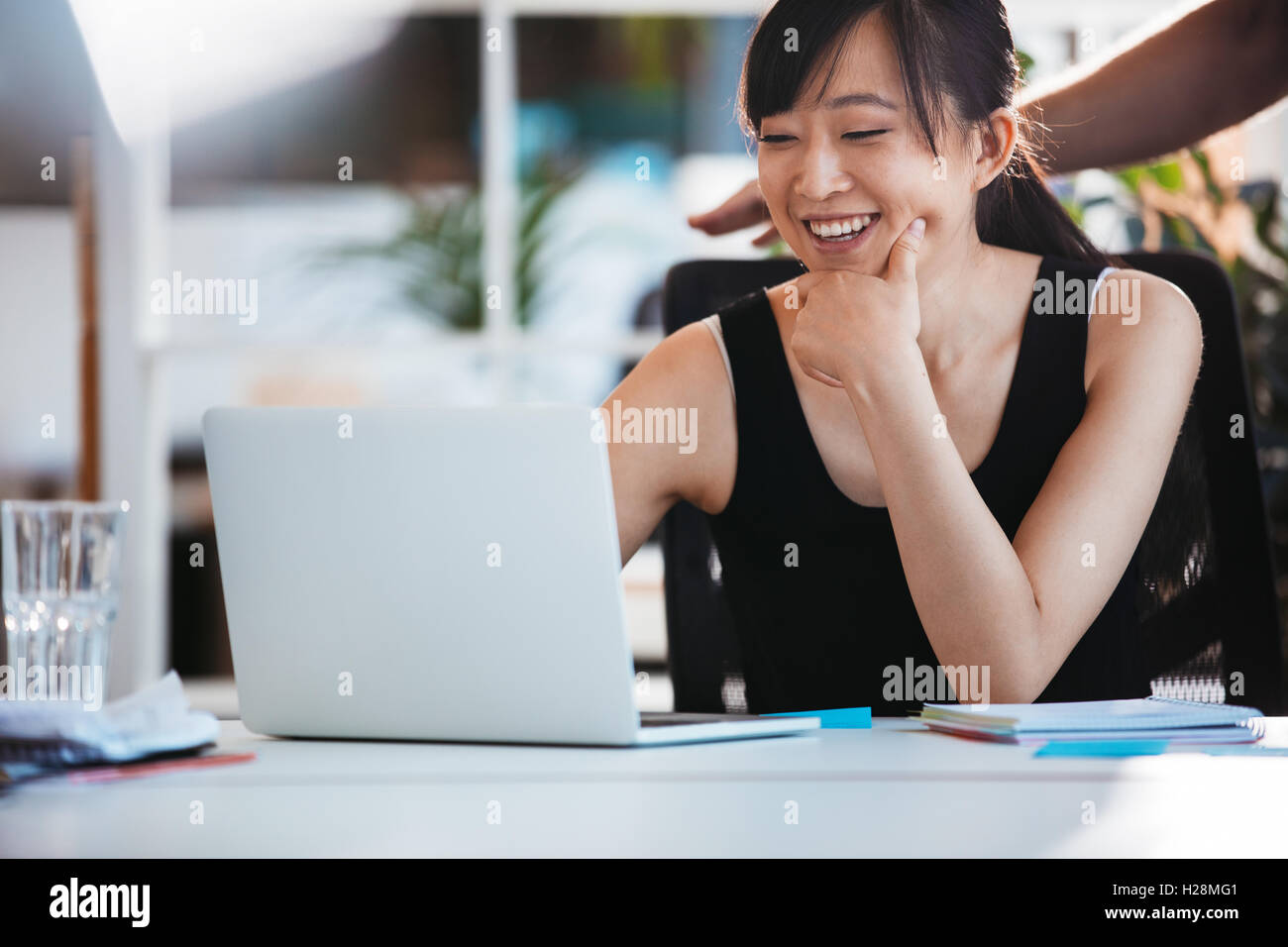 Shot of young smiling woman sitting at her desk and working on laptop. Asian female executive using laptop computer. Stock Photo
