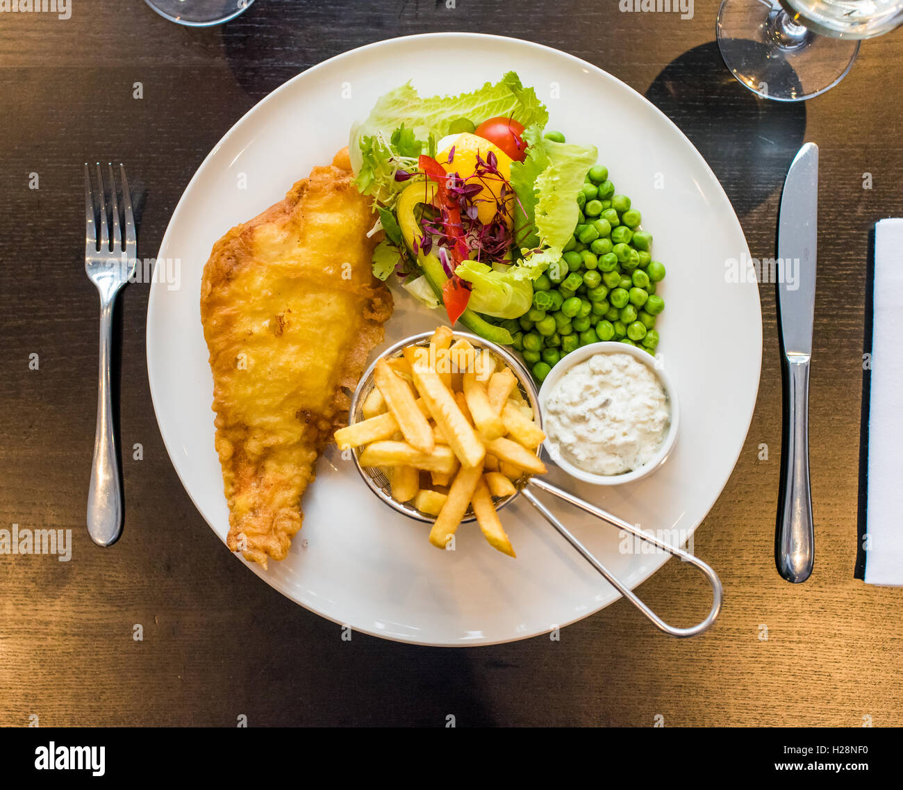 Fish and chips with peas served on a plate with salad and tartar sauce