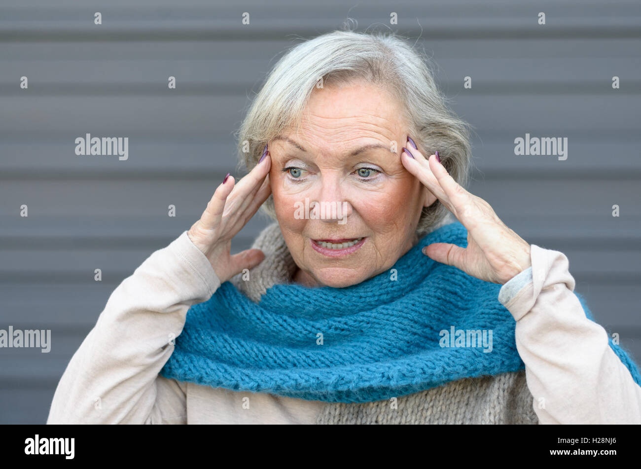 Confused and bewildered senior lady holding her hands to her temples as she looks aside, conceptual of the onset of dementia or  Stock Photo