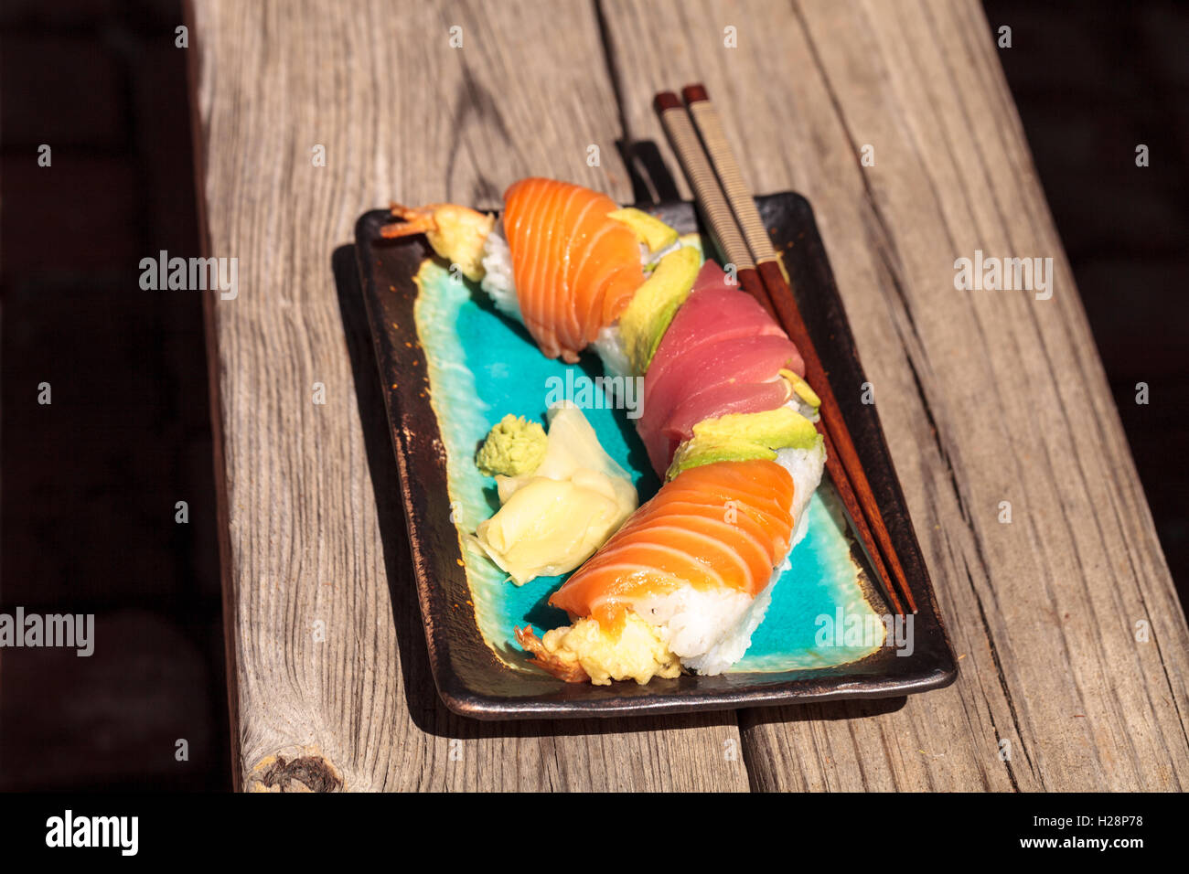 Dragon roll sushi with salmon, tuna, avocado, shrimp tempura and rice on a plate with chopsticks