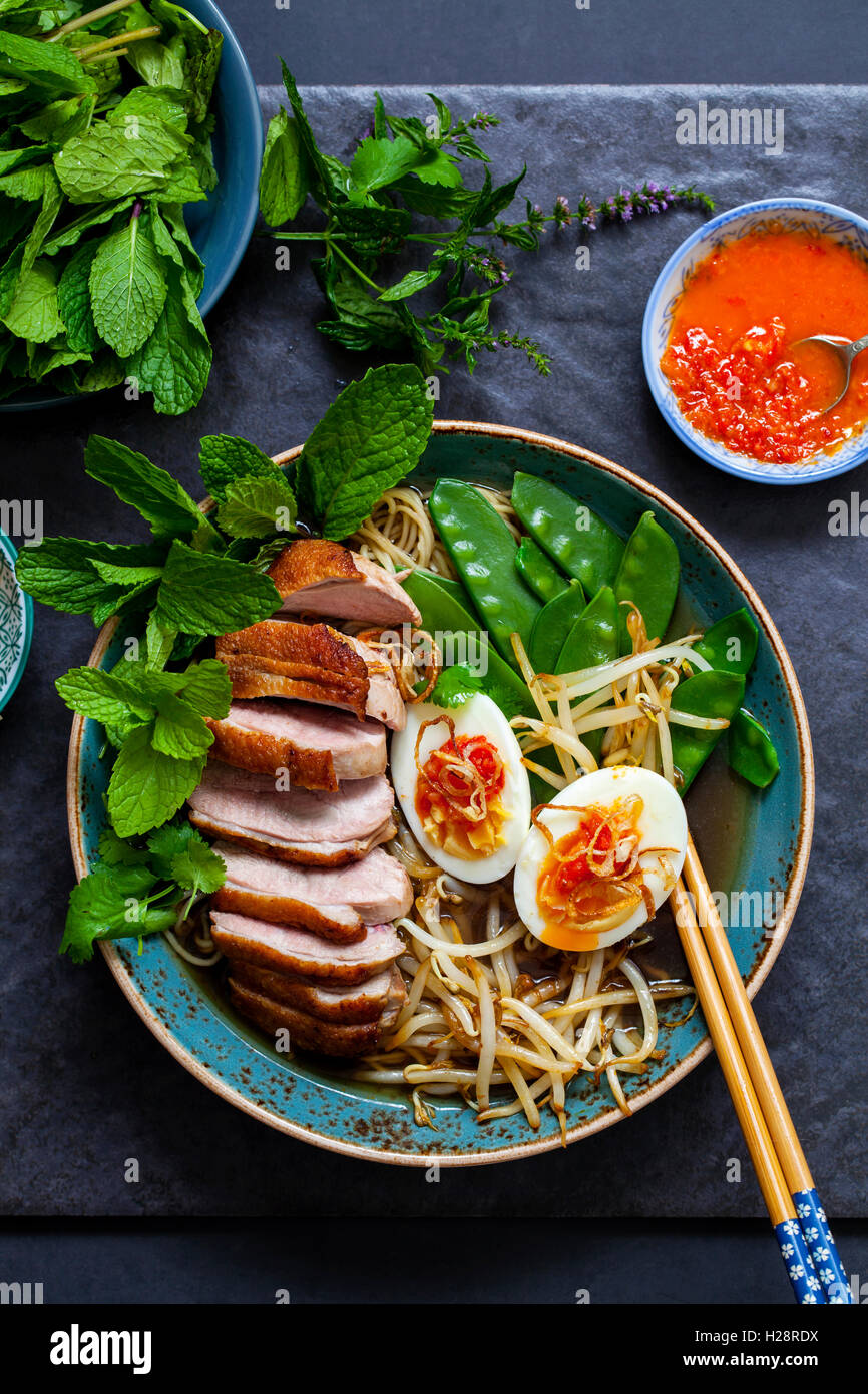 Vietnamese pho with duck with crispy skin, bean sprouts and egg, chili sauce and herbs Stock Photo