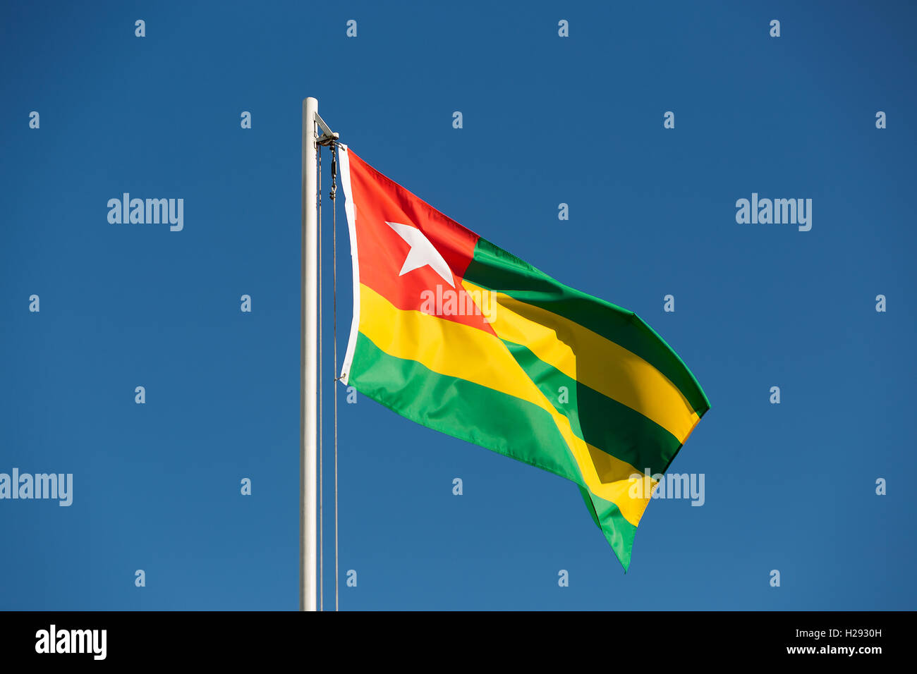 National flag of Togo on a flagpole in front of blue sky Stock Photo