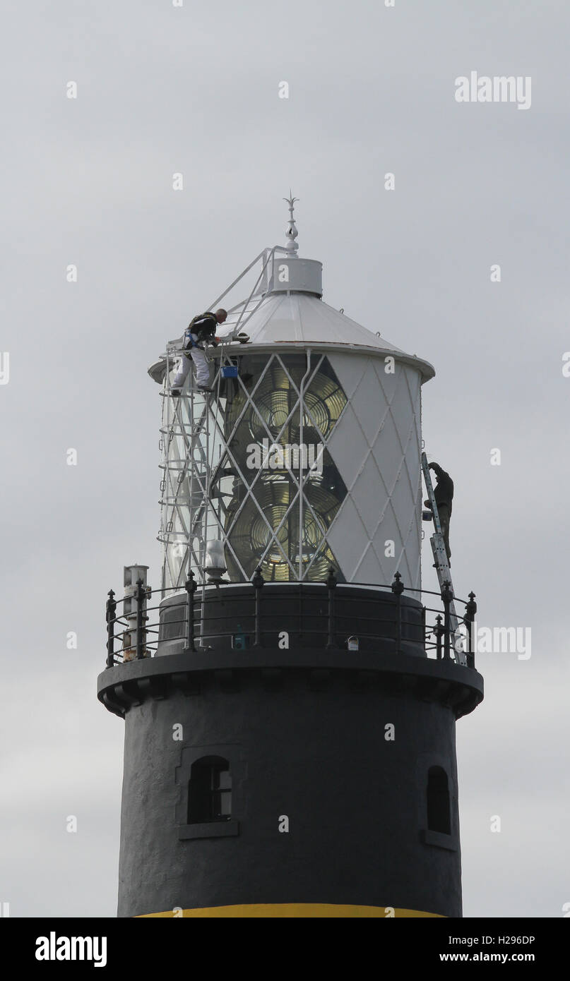 Two men on the roof of a lighthouse painting the lighthouse lamp tower on a grey day at St John's Point County Down Northern Ireland. Stock Photo