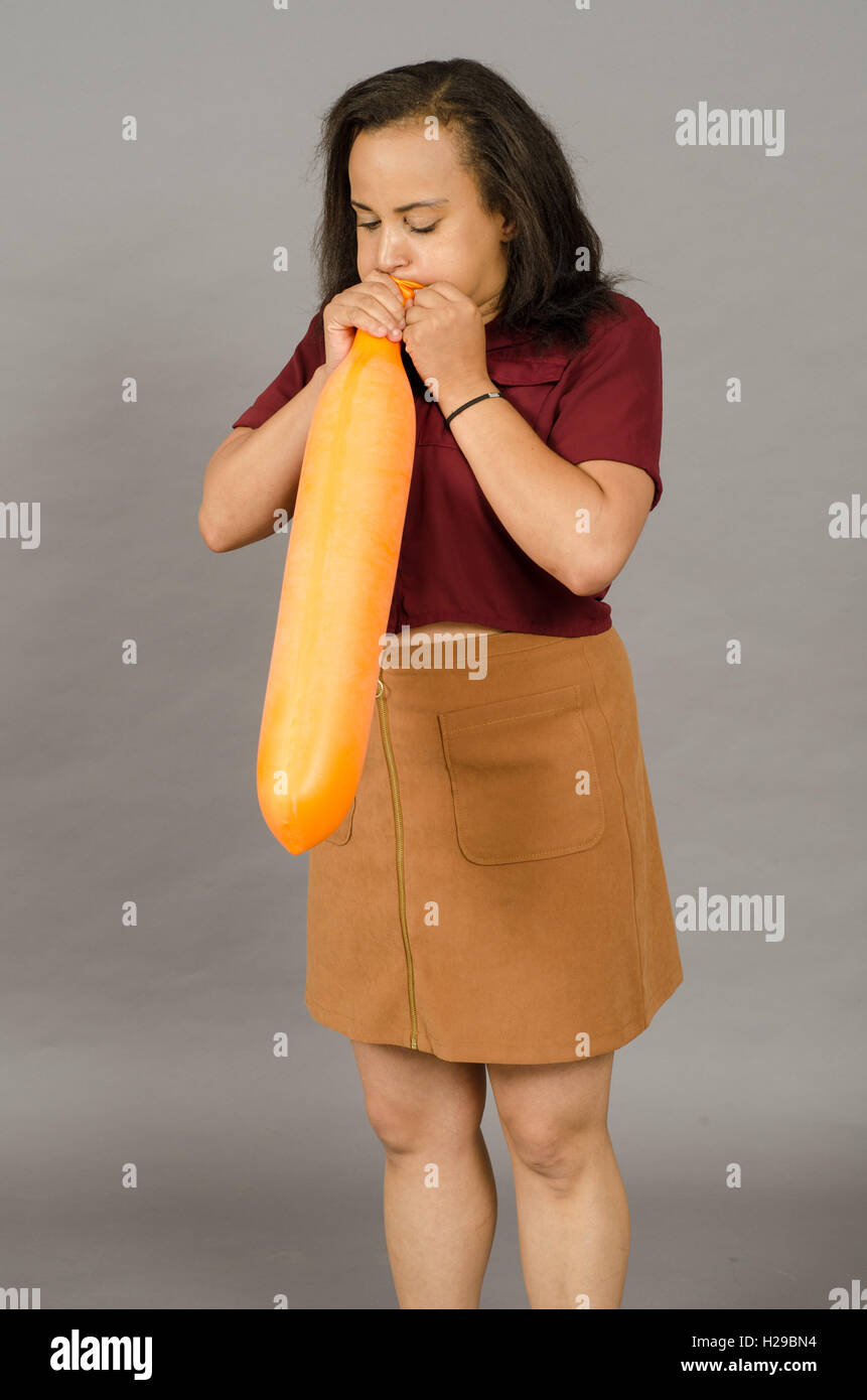 Adult adult female blowing up a huge orange long balloon Stock Photo - Alamy