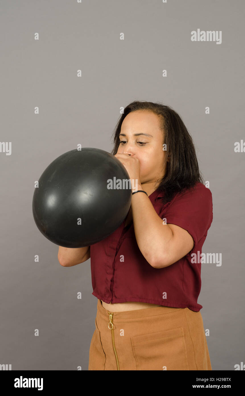 adult female blowing up a very large black balloon Stock Photo