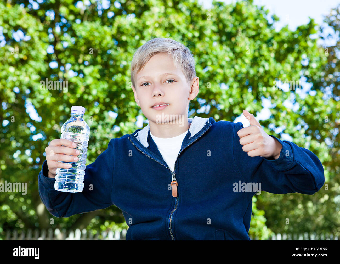 Young teenage boy with bottle of water in park sitting on the bench ...