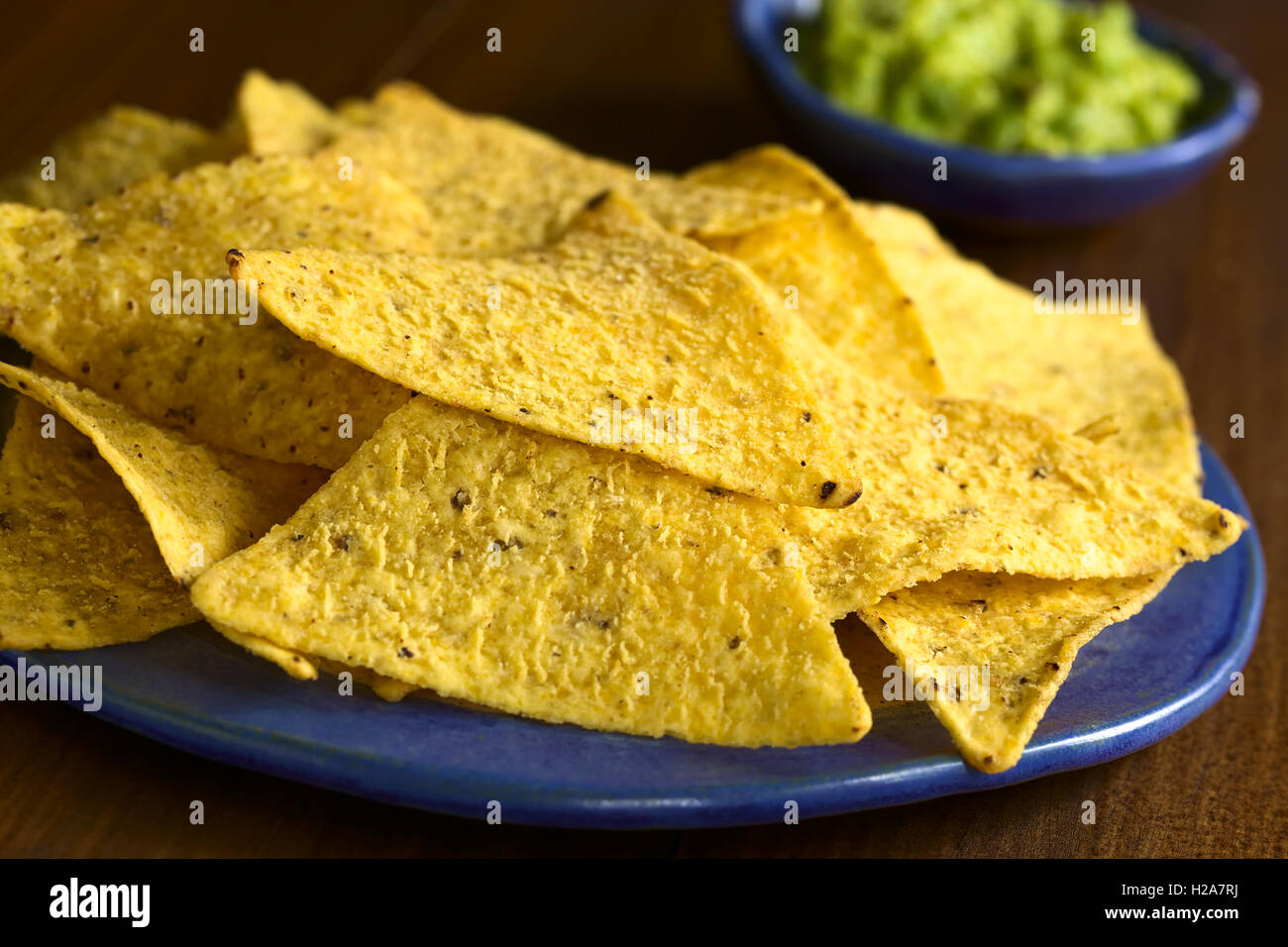 Corn tortilla chips with avocado dip in the back, photographed with