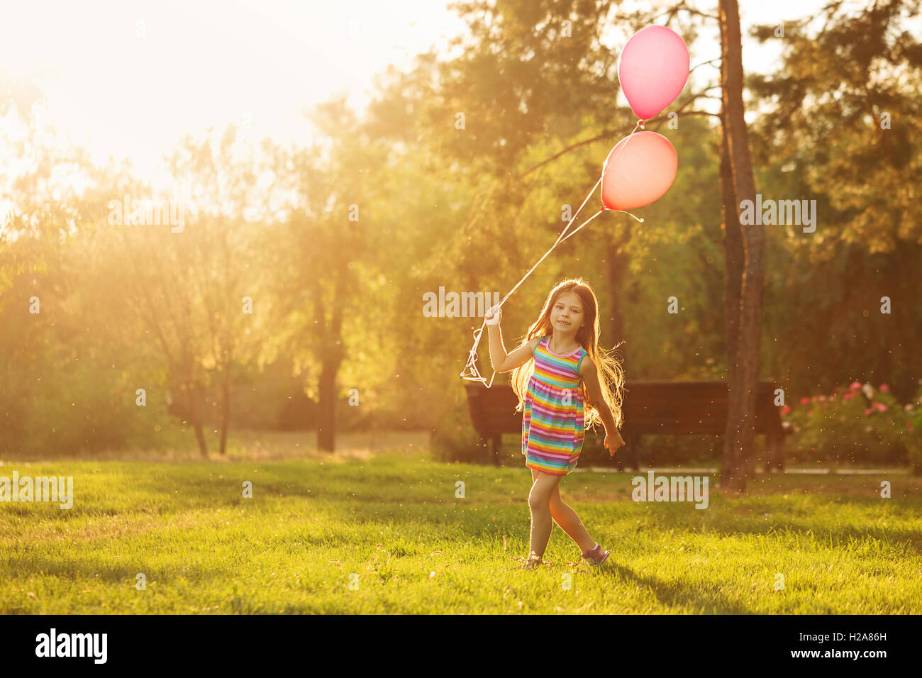 Little girl with balloons walking on the lawn in the park outdoors ...