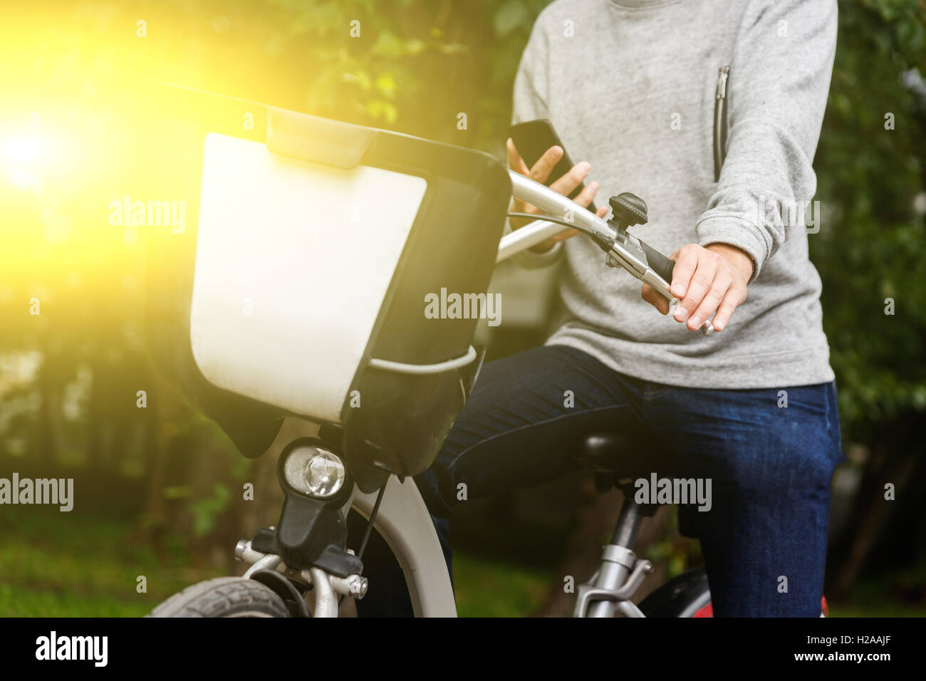Man sitting on bike with mobile phone in green area Stock Photo