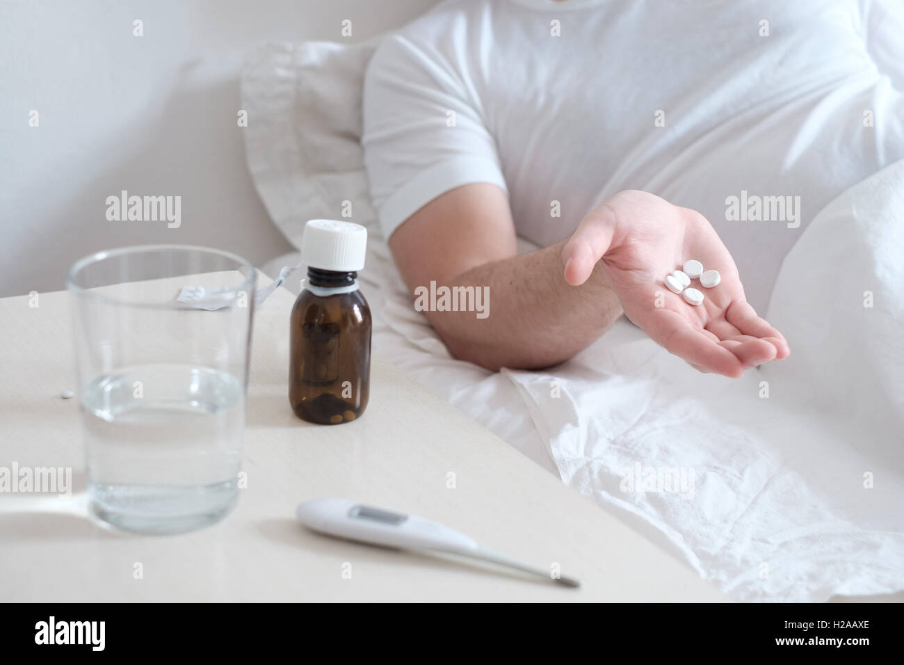 Man taking medicine pills lying in the bed Stock Photo