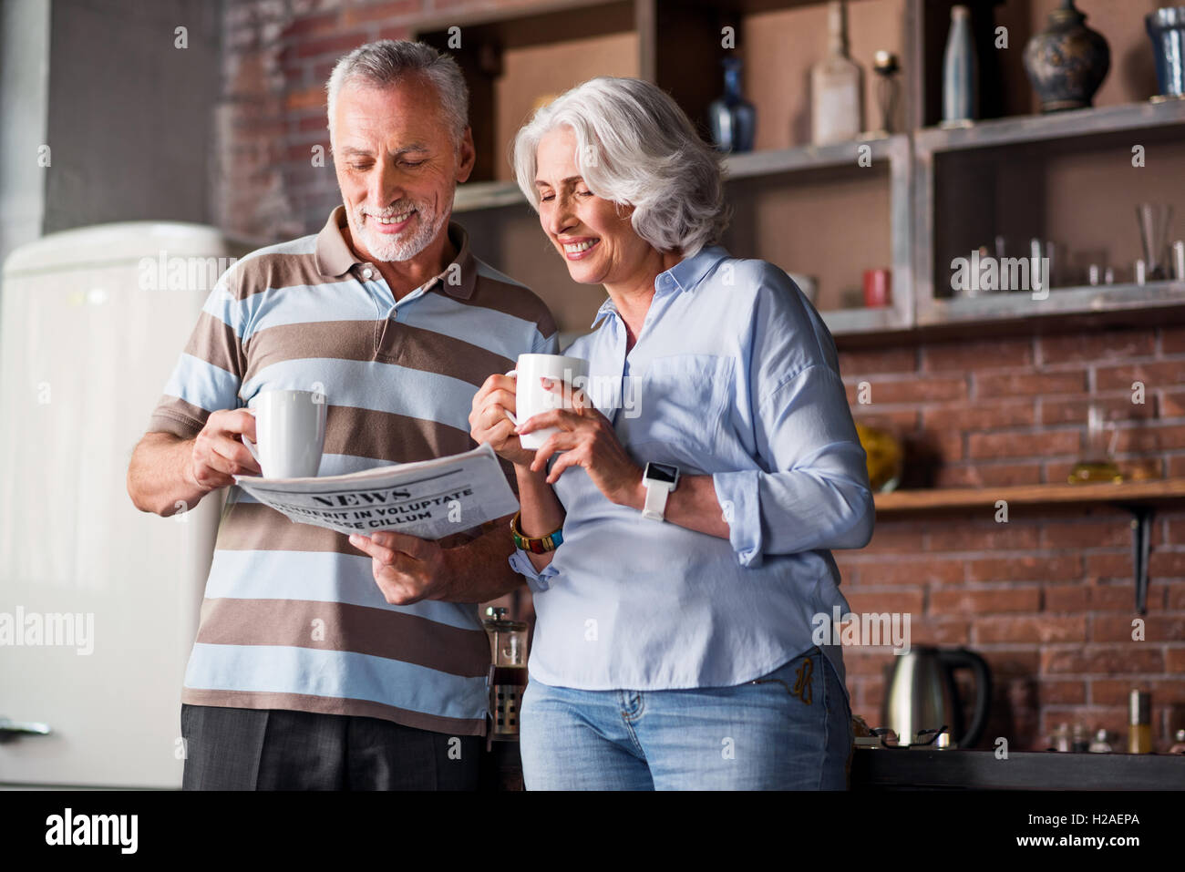 Happy classy couple in their sixties laughing at the kitchen Stock Photo