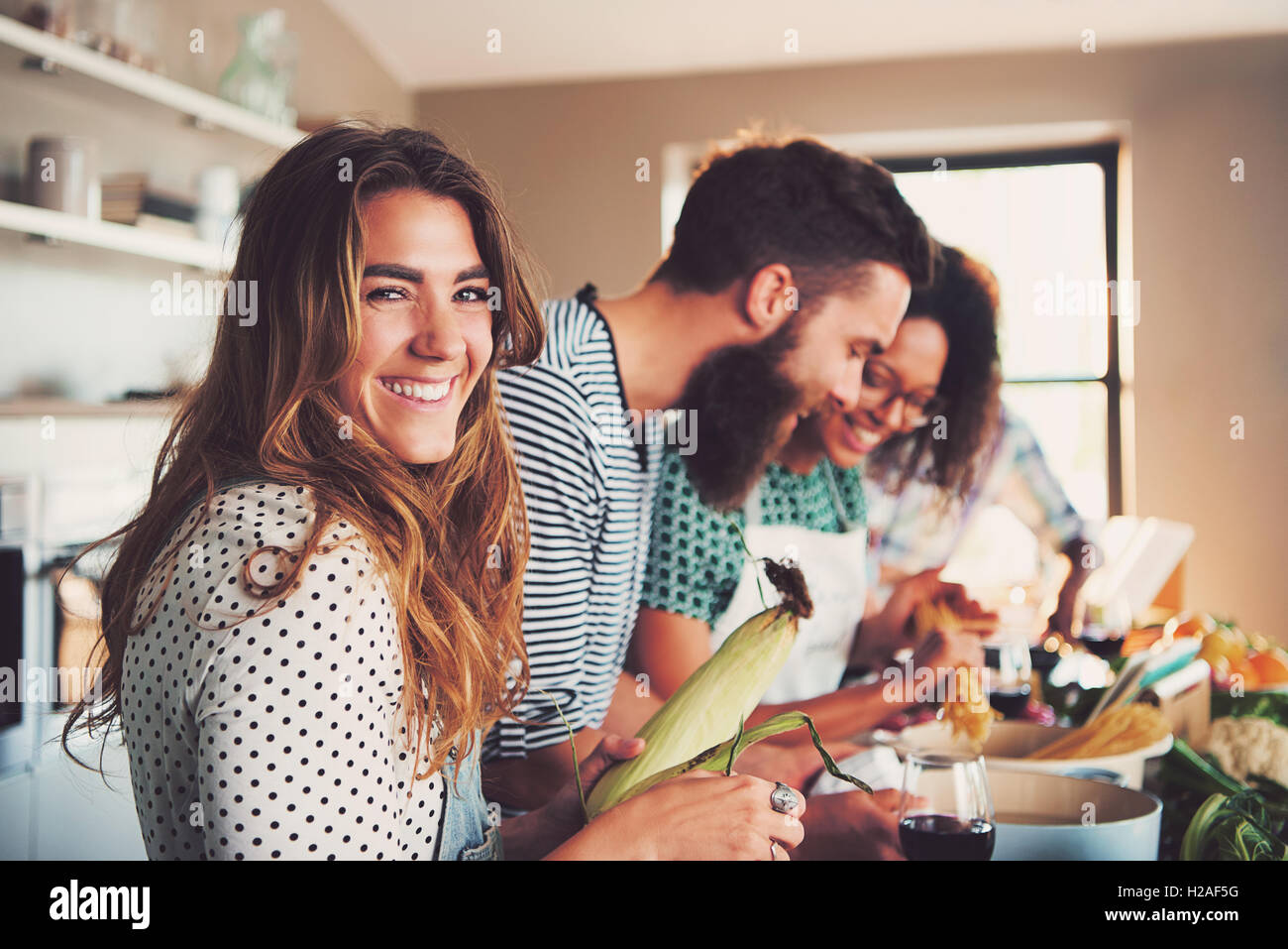 Laughing woman talking and preparing meals at table full of vegetables and pasta ready for cooking in kitchen Stock Photo